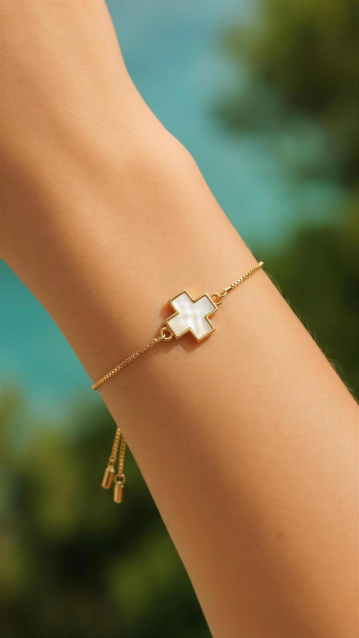 Gold bracelet with a white heart charm on a blurred natural background