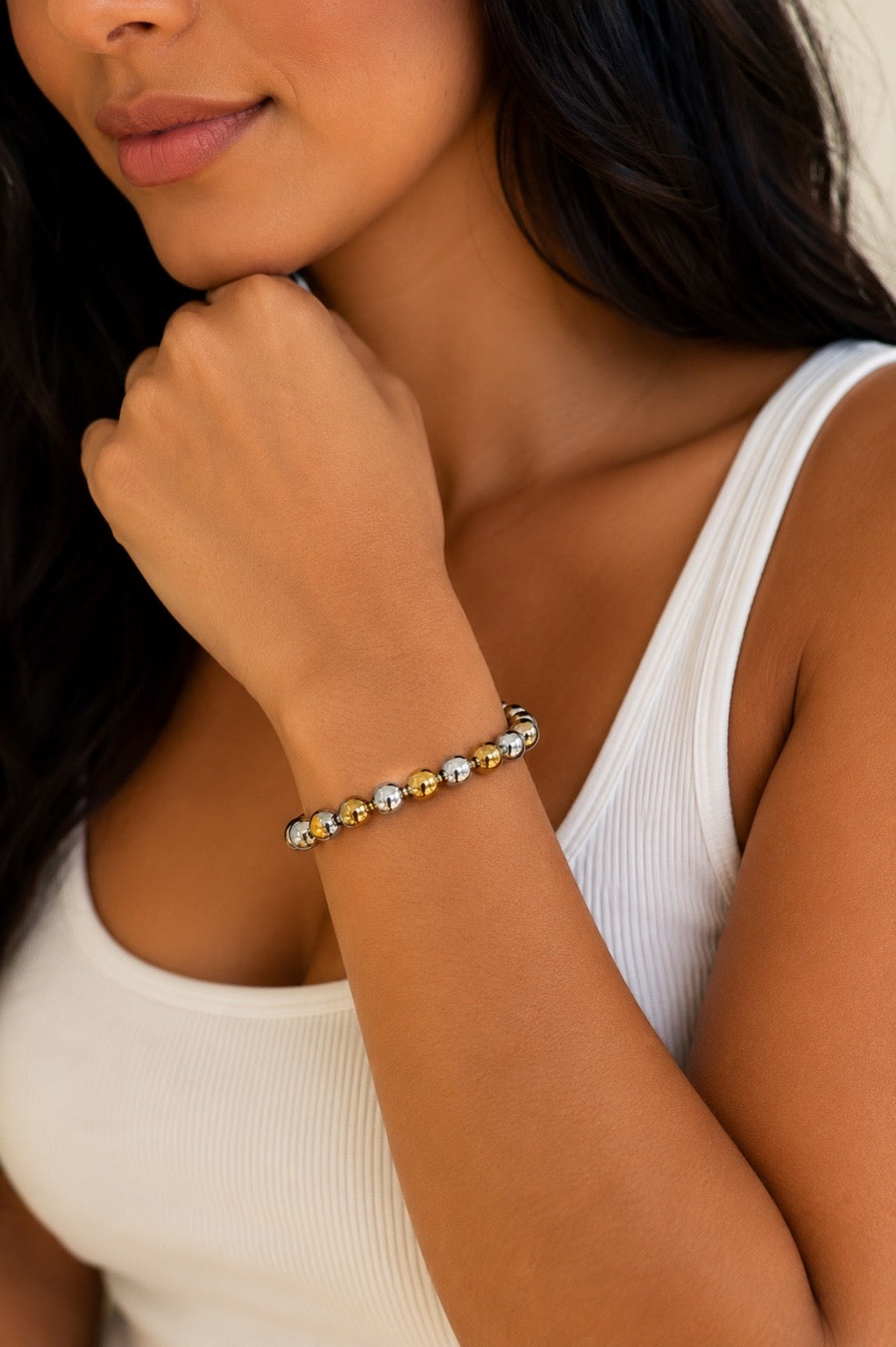 A close-up of a woman wearing a beaded bracelet on her wrist. The bracelet features alternating metallic gold and silver beads.