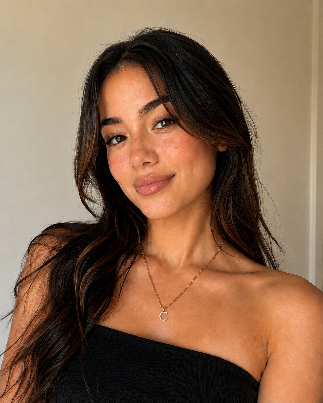 Woman with long dark hair wearing a black strapless top against a neutral background