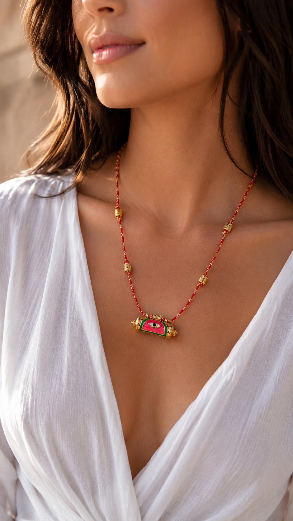A close-up lifestyle shot of a woman wearing a bohemian-style beaded necklace with a pink and green rectangular pendant, paired with a white draped top.